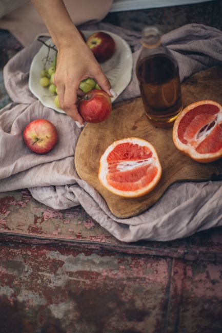 High angle of crop faceless female with manicure holding apple over textile with fruits and beverage