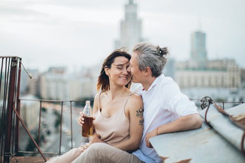 Cheerful couple in stylish clothes caressing each other while resting on rooftop of city
