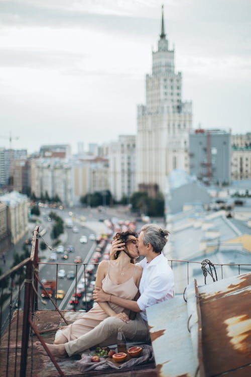 Full body of romantic couple in stylish casual clothes kissing with passion on roof during picnic