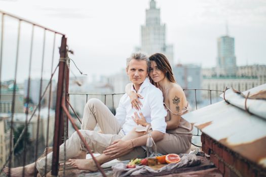 一对穿着休闲装的年轻浪漫夫妇在屋顶上依偎着，侧身望向镜头