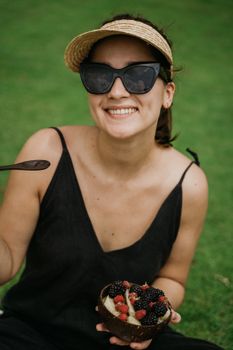 A cheerful woman in sunglasses enjoys a fresh berry bowl on a sunny day.