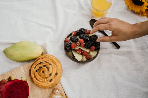 Person Picking Fresh Berries from Wooden Bowl 