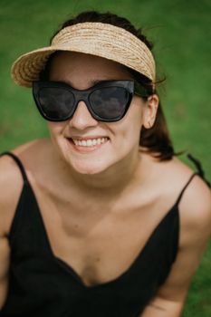 Smiling woman outdoors in sunglasses and sun hat, enjoying a sunny day.