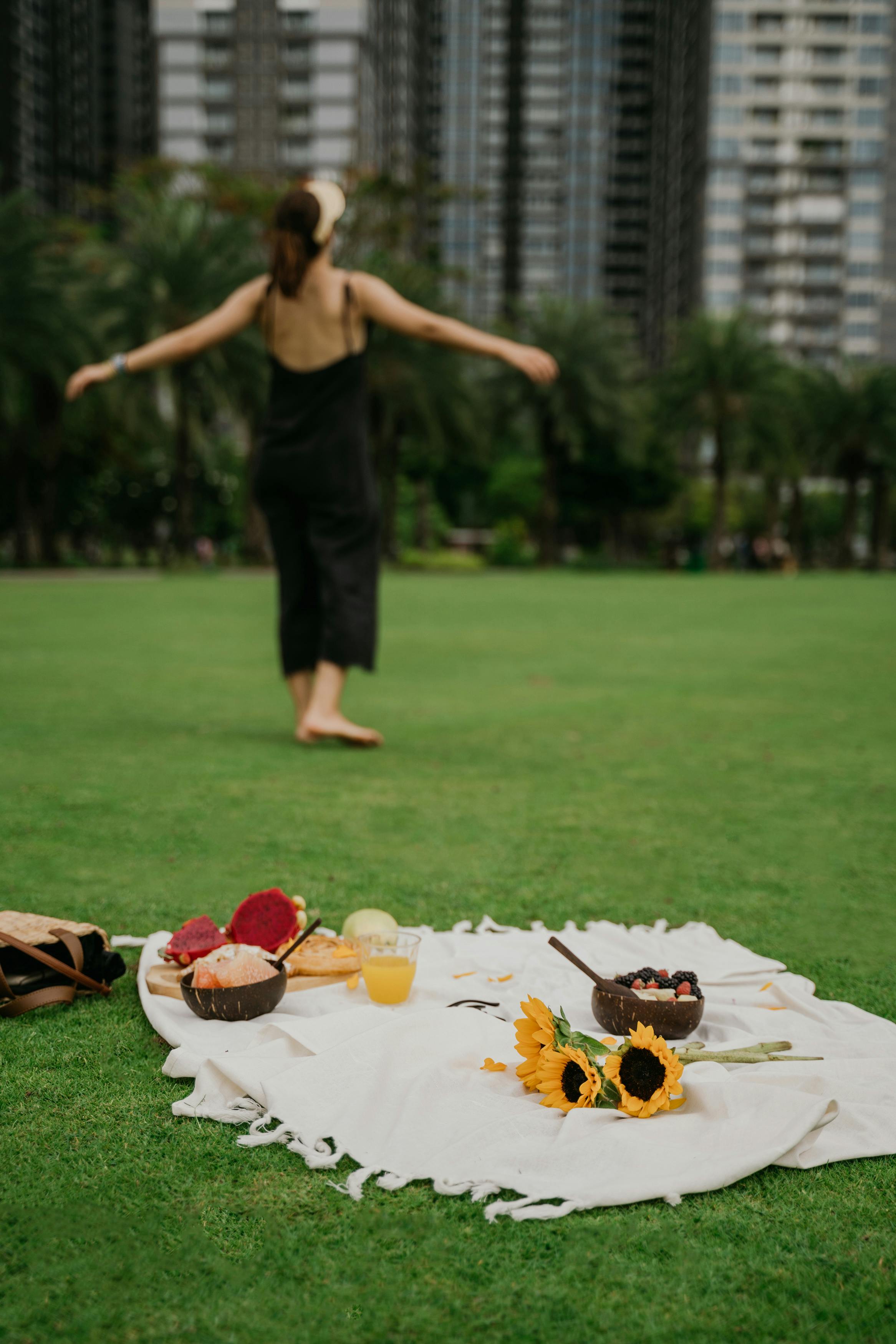 一名妇女在城市公园的草地上，一边享用零食，一边欣赏向日葵，享受着宁静的野餐时光