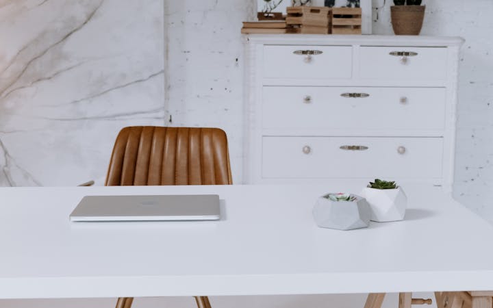 A stylish workspace featuring a clean white desk, leather chair, and decorative elements in a modern office setting.