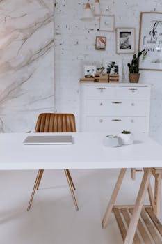 A stylish workspace featuring a clean white desk, leather chair, and decorative elements in a modern office setting.