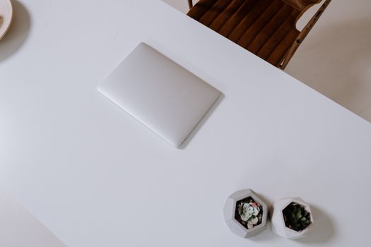 A modern, minimalist white desk featuring a closed laptop and succulents.