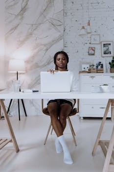 Young woman using laptop in a stylish home office setting, showcasing modern work-from-home lifestyle.