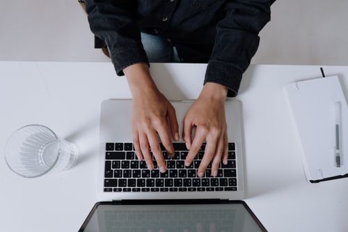 Free Hands typing on a laptop keyboard viewed from above, capturing a modern work environment. Stock Photo