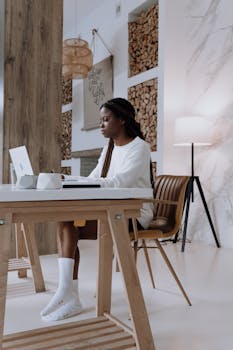 A woman working on her laptop in a modern, minimalist home office interior.