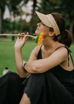 一名女子坐在公园的向日葵旁，戴着遮阳帽，享受着平静的时刻