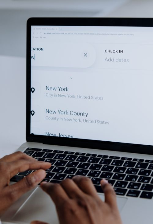Free Hands typing on a laptop near New York location search screen. Stock Photo