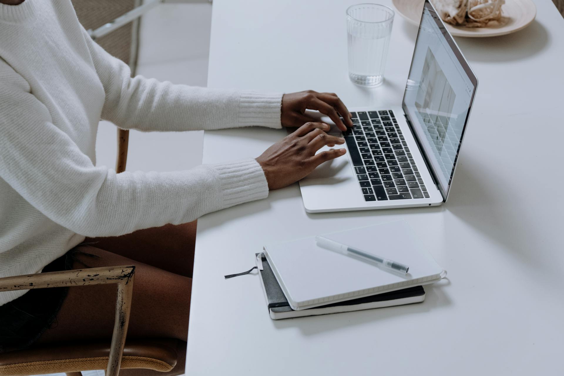 A person typing on a laptop in a minimalistic home office setting, capturing modern work culture.