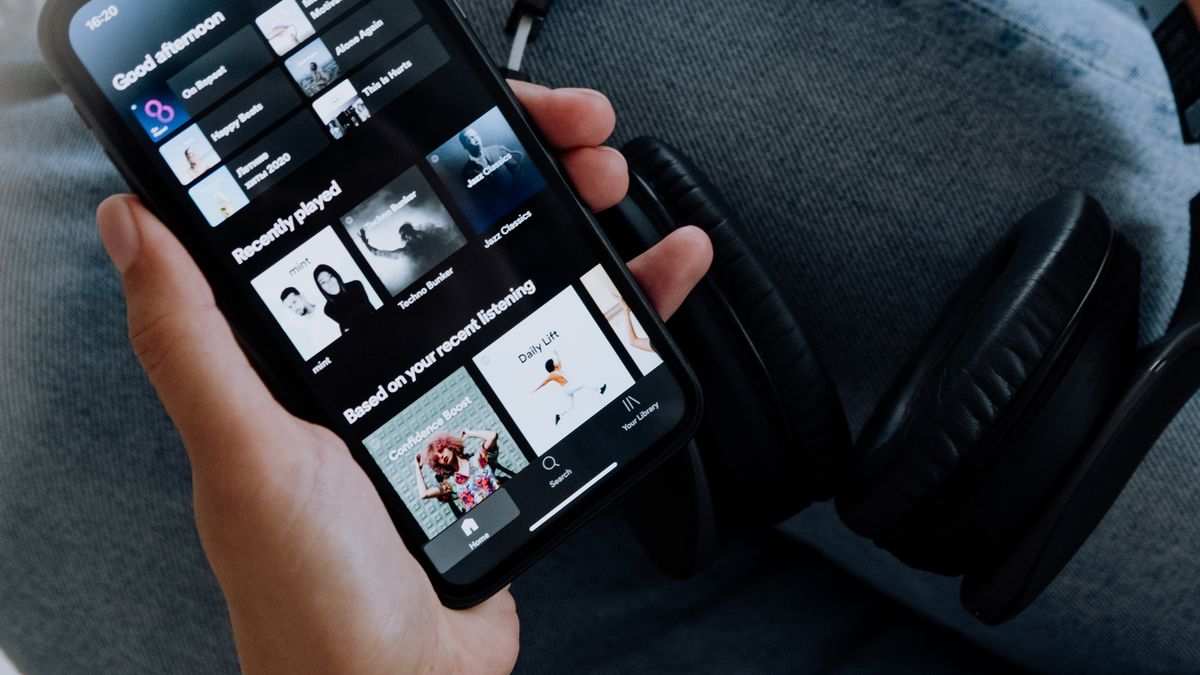 Person browsing a music streaming app on a smartphone with headphones