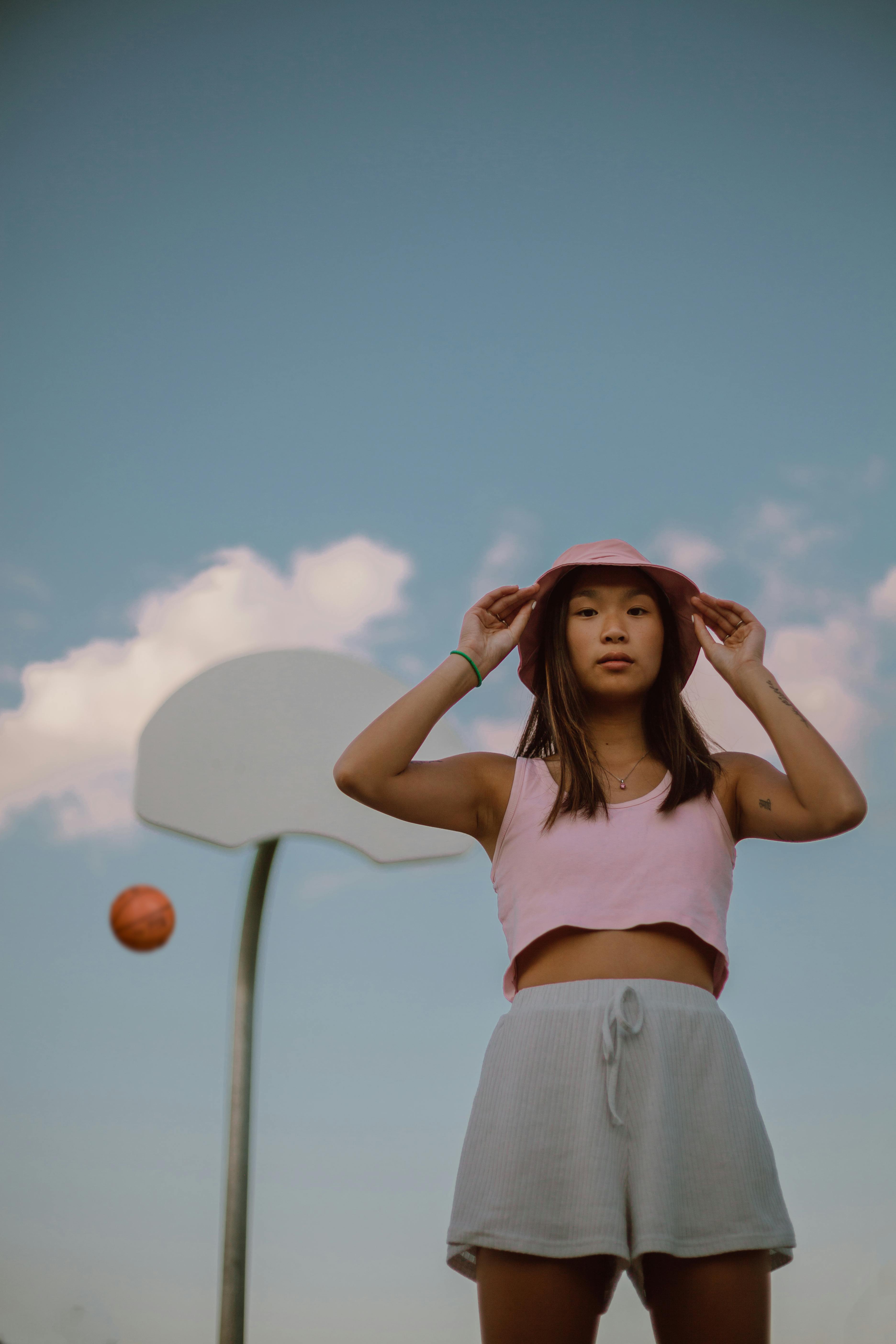 young ethnic woman touching hat while standing on sports ground