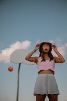 Asian woman standing confidently on a basketball court, under a bright blue sky.