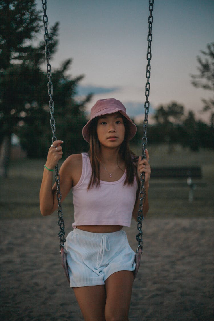 A Woman Wearing Tank Top And Shorts Sitting On The Playground Swing