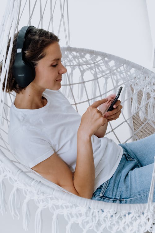 Free Woman in White Crew Neck T-shirt and Blue Denim Jeans Holding Smartphone Stock Photo
