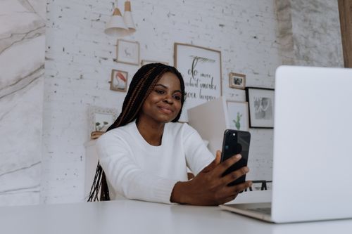 Free A young woman having a video call at her home office with a smartphone, displaying positive emotions. Stock Photo