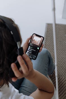 A young woman wearing headphones, relaxing at home, listens to music on her smartphone.