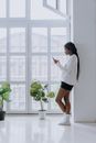 Woman in White Long Sleeve Shirt and Black Skirt Standing Beside Green Potted Plant