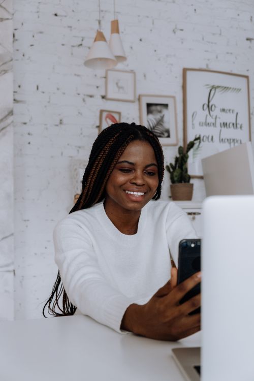 Free A smiling young woman with braids enjoying a video call in her minimalist apartment. Stock Photo