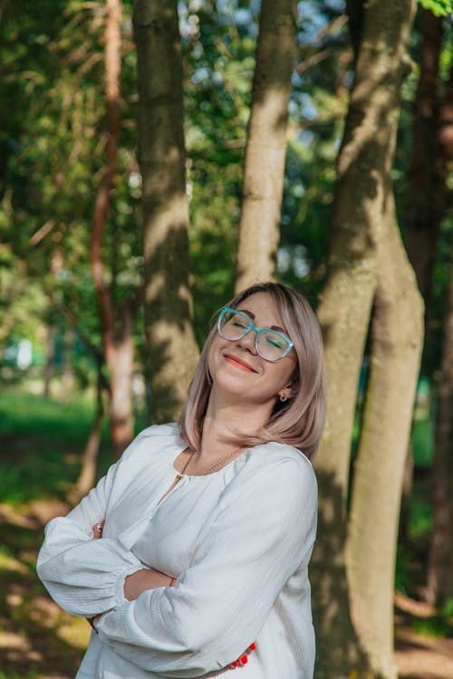 Content dreamy woman in eyewear near trees in park