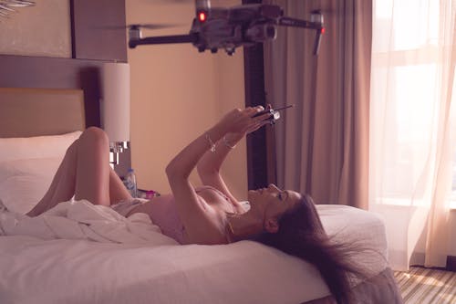 A Woman Lying in Bed and Playing with a Drone