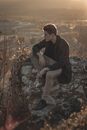 Man in Black Jacket and Brown Pants Sitting on Rock