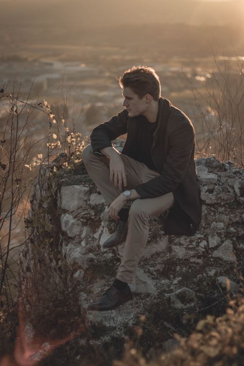 Free Man sitting on a rocky cliff at sunset in Postojna, Slovenia. Serene and reflective moment. Stock Photo
