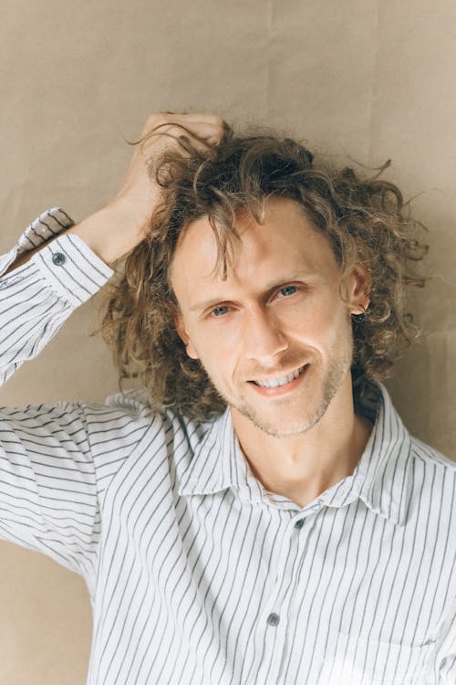 Free Close-Up Shot of a Curly-Haired Man in Striped Button-Up Shirt Smiling while Looking at Camera Stock Photo