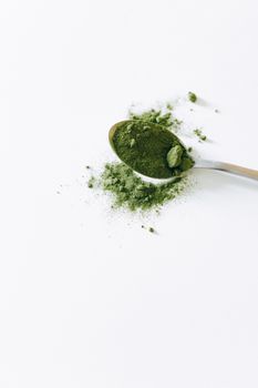 白色背景上，银勺顶视图覆盖着有机抹茶粉