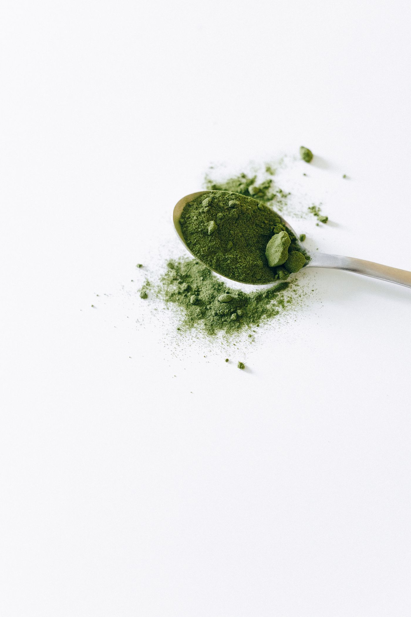 Matcha powder with small clumps on a metal spoon against a white background