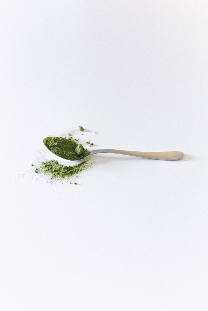 A spoon with green matcha powder spilled on a white surface, close-up view.