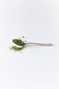 一把装有绿色抹茶粉的勺子洒在白色表面上，特写镜头