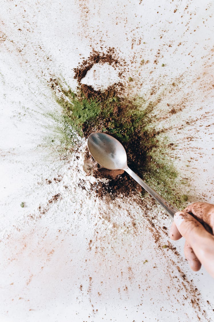 A Person Holding A Stainless Spoon Over The Spice Powder