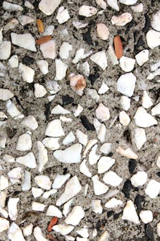 Abstract textured surface with white and gray stones set in cement, ideal for design and decor use.