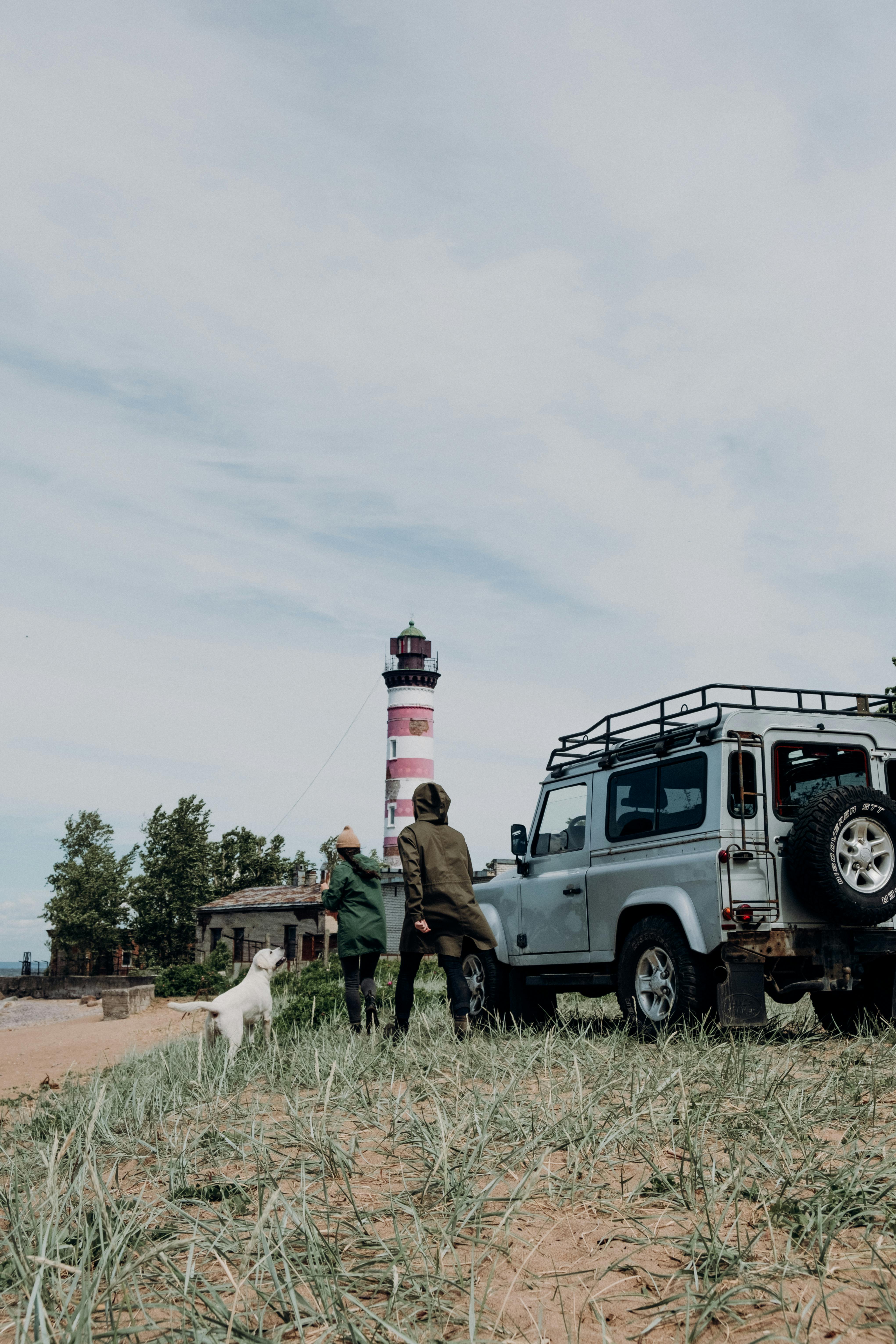 一对夫妇带着他们的狗，在一辆坚固的车辆旁的红白灯塔附近探索