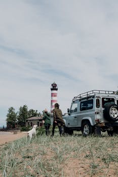 一对夫妇带着他们的狗，在一辆坚固的车辆旁的红白灯塔附近探索