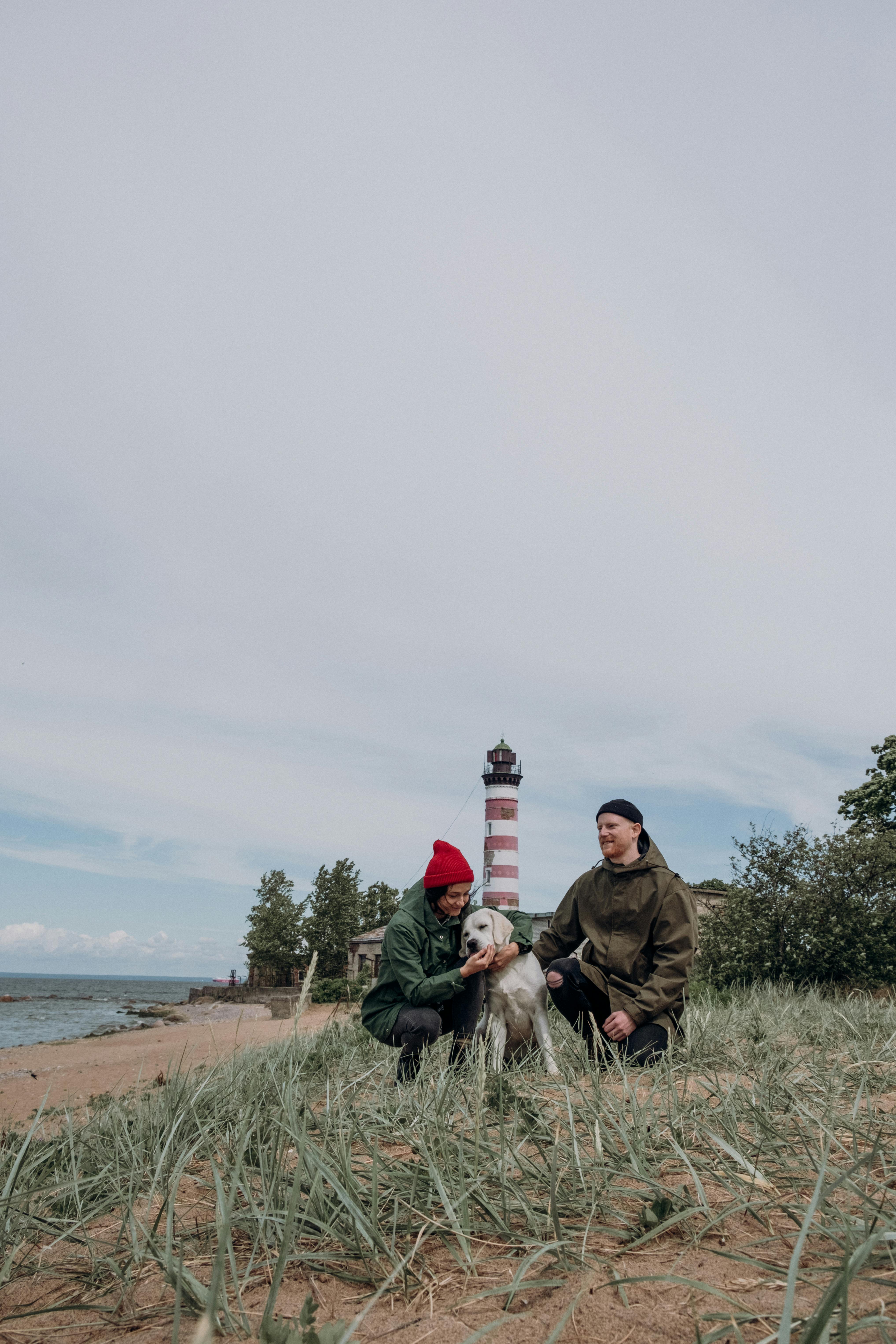 一对夫妇带着他们的狗在经典灯塔附近的海滩上散步