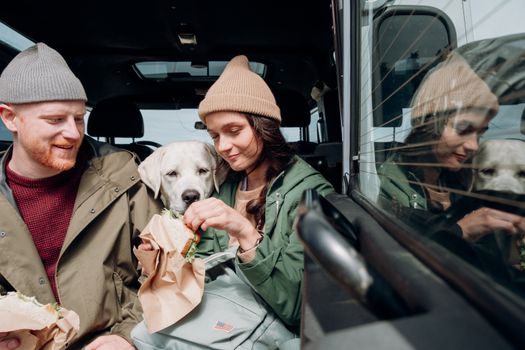 寒冷的日子里，一对夫妇和他们的拉布拉多猎犬在车里享用晚餐