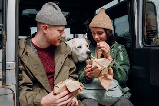 A couple enjoys sandwiches with their dog during an outdoor adventure.