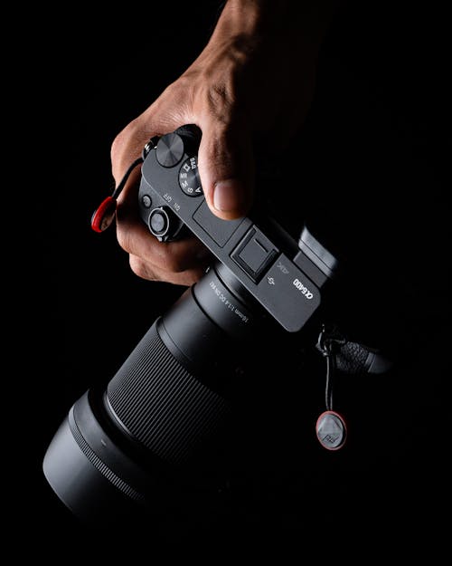 From above anonymous person holding modern professional photo camera with lens on black background