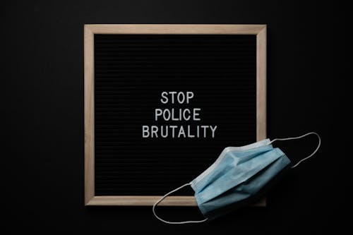 Top view composition of framed black image with white text Stop Police Brutality near medical protective mask