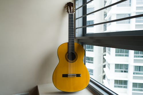 Acoustic Guitar on White Wall Beside the Window