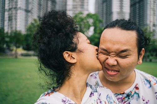 Free A couple shares a playful, affectionate moment in a park with skyscrapers in the background. Stock Photo