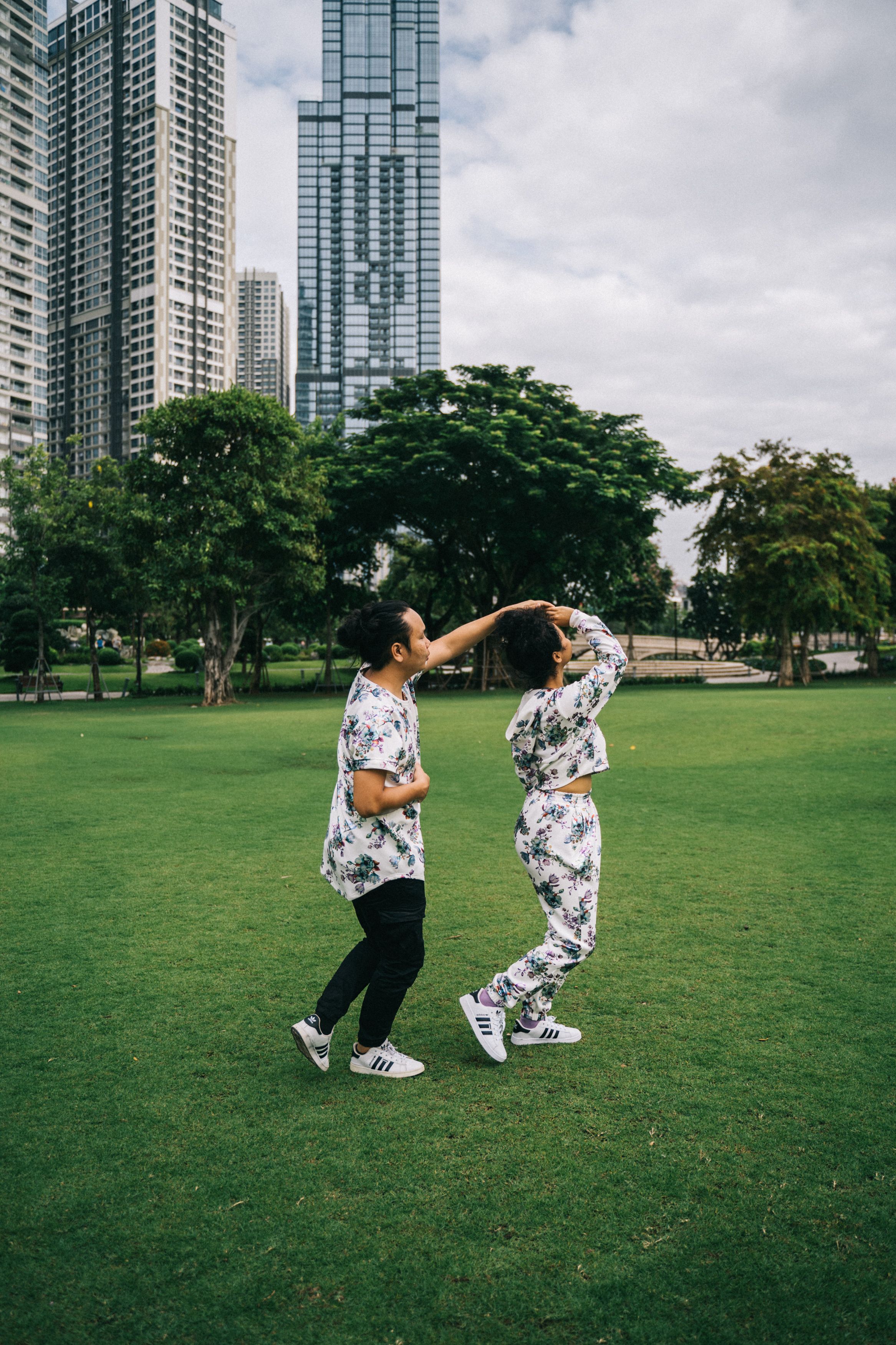 一对夫妇在城市公园里开玩笑地跳舞，四周高楼林立，绿意环绕