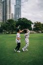 一对夫妇在城市公园里开玩笑地跳舞，四周高楼林立，绿意环绕