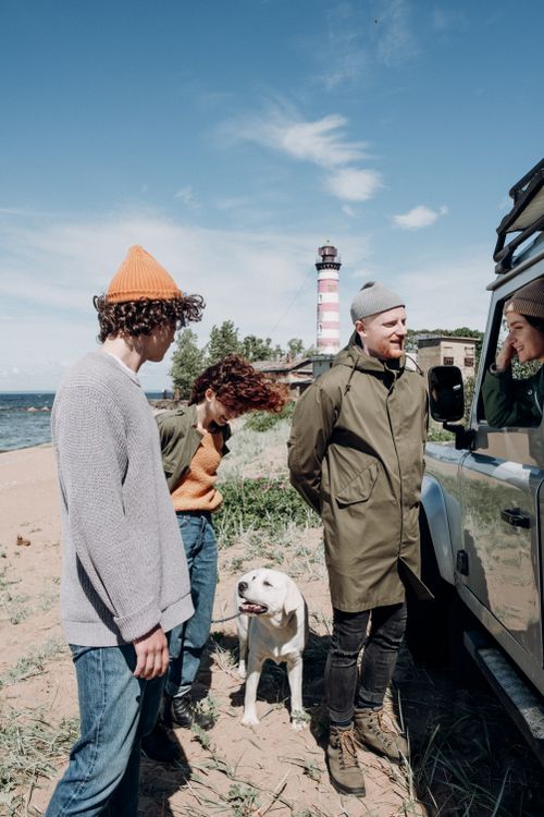 Free Group of friends with a dog at a beach near a lighthouse, enjoying a sunny day. Stock Photo