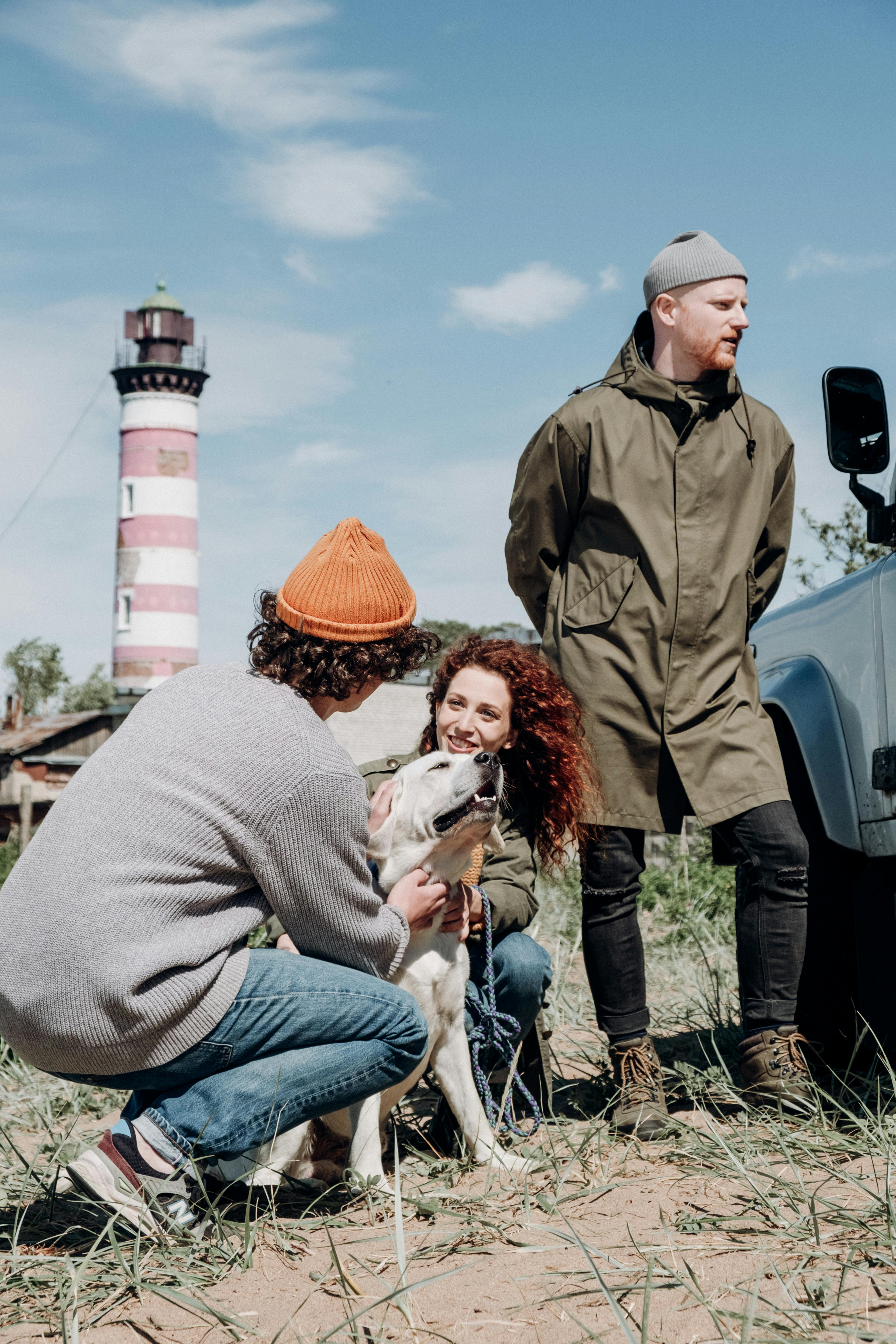 一群人在灯塔附近带着狗散步，在蓝天下微笑着享受户外时光